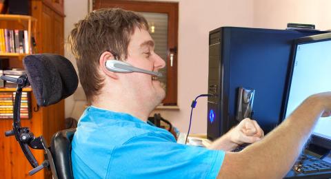 person wearing assistive headset pointing at computer