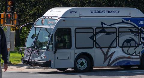 Picture of one of the wildcat campus busses with a student walking in front