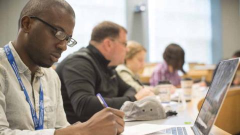 Student taking notes while working on laptop