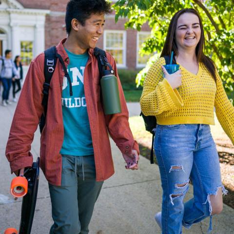 Two students smiling and chatting while walking through campus
