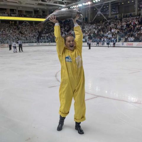Student standing on the ice inside the Whitt holding up a fish while cheering
